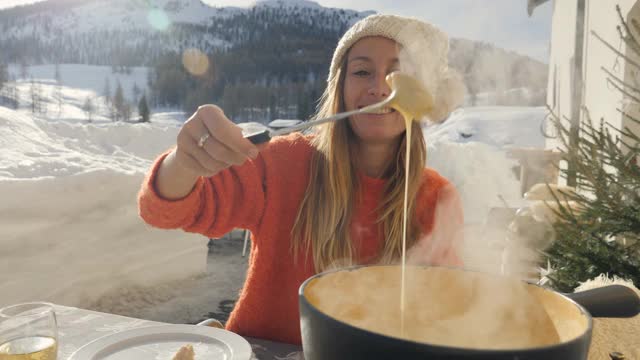 快乐的年轻女子吃芝士火锅在瑞士享受阿尔卑斯山和雪山在冬季假期。人们的饮食传统地方观念视频素材