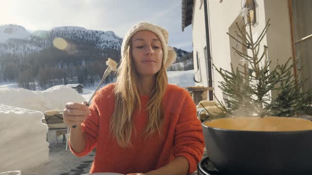 快乐的年轻女子吃芝士火锅在瑞士享受阿尔卑斯山和雪山在冬天视频素材