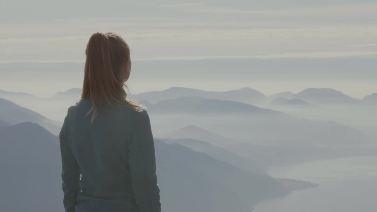 女徒步旅行者站在山顶，双臂张开。年轻女子在徒步旅行中举起双臂俯瞰壮观的山脉视频素材