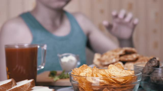 饥饿的小手从盘子里拿起脆脆的金色薯片。晚餐中的垃圾食品视频素材