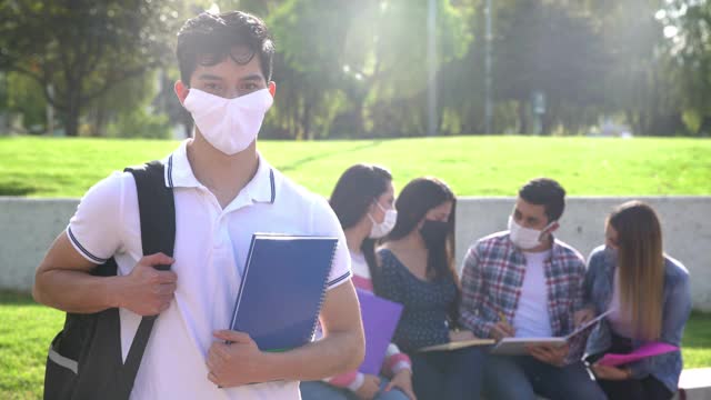 一名年轻的男学生在大学校园里拿着一个笔记本，戴着一个保护面罩视频素材