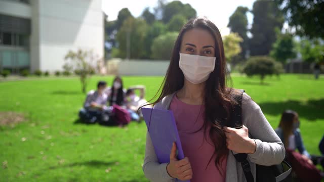 拉丁美洲年轻女学生拿着她的背包和一个文件夹面对相机戴着保护面罩在大学视频素材