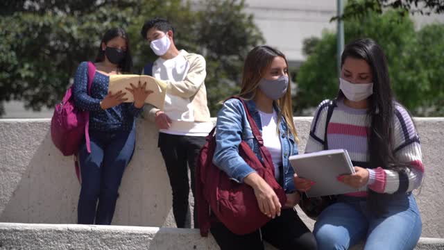 朋友们一起学习，然后问候一个男性朋友，碰撞肘部，挥手，所有人都戴着防护口罩视频素材