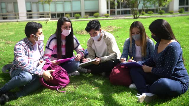 一群年轻的朋友在大学校园里坐在草地上学习，都戴着防护口罩视频素材