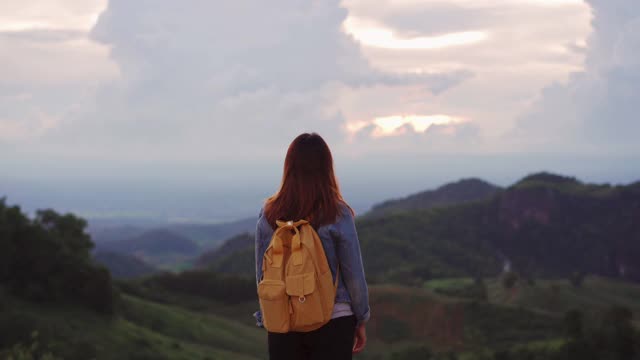 快乐的年轻女子旅行者放松和看美丽的日落在山顶视频素材