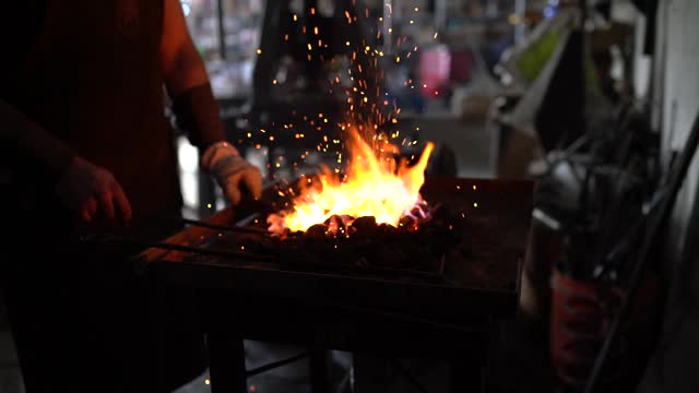 一个技术熟练的铁匠在他的车间里工作，同时扇他的火达到更高的温度。视频素材