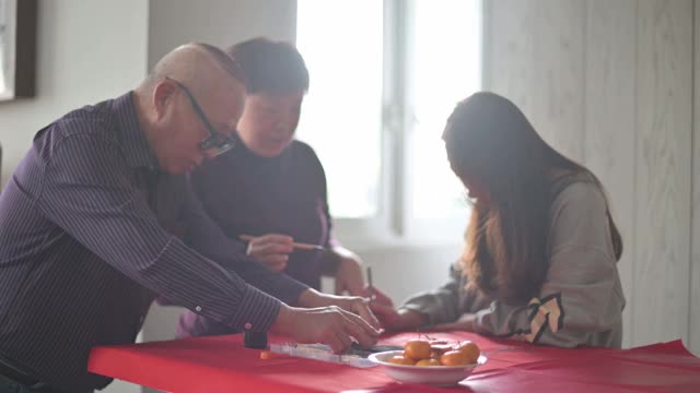 亚洲华人家庭在红纸上书写中国书法，以求繁荣，准备中国新年的家庭装饰视频素材