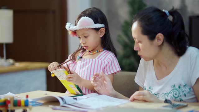 亚洲母亲教家庭作业为她的女儿，而工作在家里的办公室视频素材