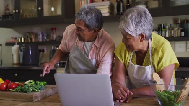 高级混合种族夫妇使用笔记本电脑准备食物在厨房视频素材