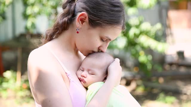 小男孩睡在妈妈的胸口上。母亲把睡着的婴儿搂在怀里，轻轻地吻着孩子视频素材