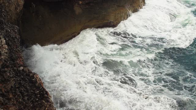 海浪拍打着深棕色的岩石悬崖，慢镜头视频素材