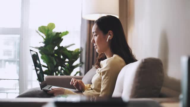 亚洲女商人在家办公，坐在沙发上用笔记本电脑开视频会议视频素材