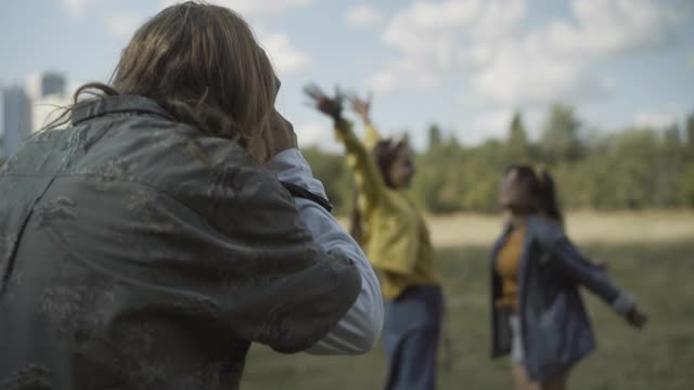 一个面目全非的男人在户外给两个快乐的嬉皮女人拍照。积极放松的白人妇女和男子在阳光明媚的夏天玩。60年代的休闲和反主流文化。视频素材