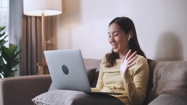 亚洲女商人在家办公，坐在沙发上用笔记本电脑开视频会议视频素材