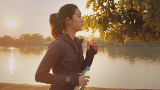 迷人的亚洲少女在公园里跑步。年轻女子晨跑锻炼。视频下载