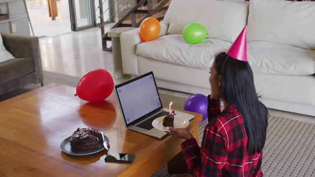 混血儿女人用笔记本电脑有生日视频聊天拿着一个蛋糕视频素材