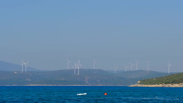 海上的帆船和山顶上的风车为背景。两个人在海上练习小小的航行。视频下载