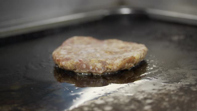 为芝士汉堡烹制牛肉和猪肉馅饼。肉在厨房烤。油滴，烟雾缭绕。视频素材