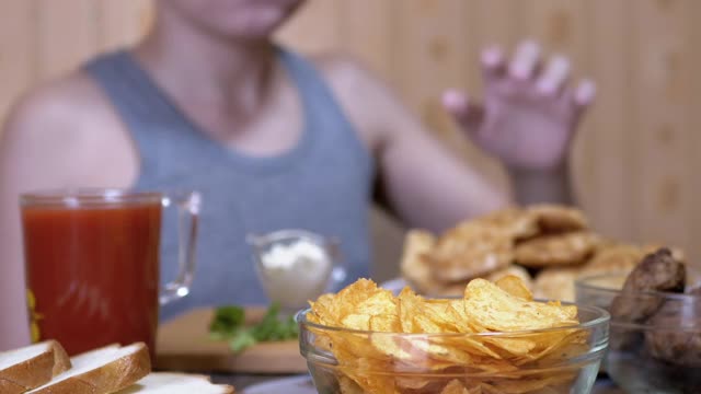 饥饿的小手从盘子里拿起脆脆的金色薯片。晚餐中的垃圾食品视频素材