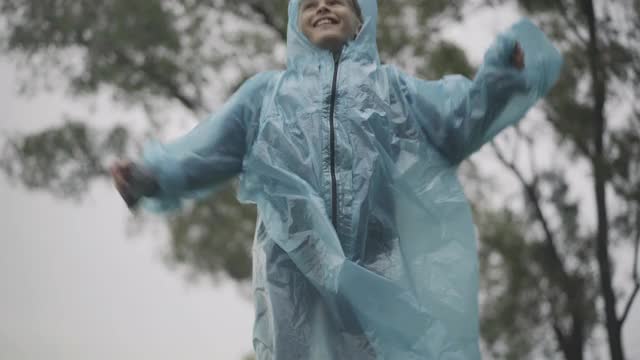 快乐的白人男孩的肖像跳跃和欢呼雨在户外。可爱的白人学生穿着雨衣玩在雨天的夏天。童年的快乐视频素材