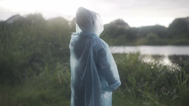 小白种人男孩的剪影伸出手，接住雨滴。快乐的学童在雨衣享受雨天夏天日落户外。生活方式和天气概念视频素材