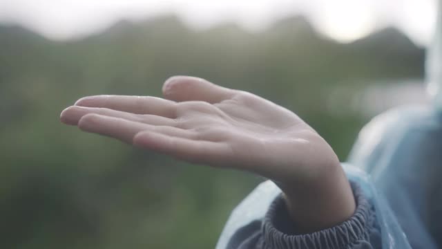 小女性白种人的手捕捉雨滴在日落户外的特写。一个面目全非的女孩在享受夏天多雨的天气。自然与童年概念视频素材