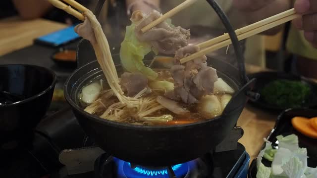 在一家日本餐馆里，餐桌上的每个人都用筷子从涮锅里抓食物。视频素材