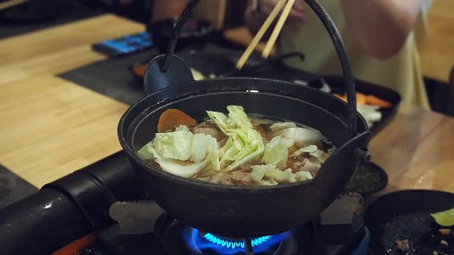 在一家日本餐馆里，一位妇女用筷子把花椰菜放进了涮锅里。视频素材