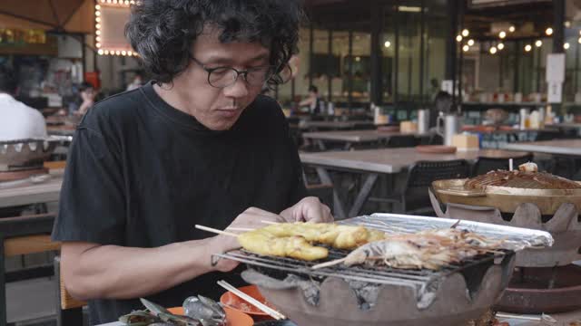 40-50岁的亚洲男性配以著名的海鲜泡芙烧烤，在泰国街头广受欢迎的海鲜美食。视频素材