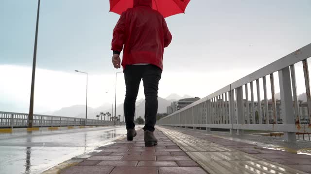 一个人穿着红色雨衣，拿着雨伞走在街上视频素材