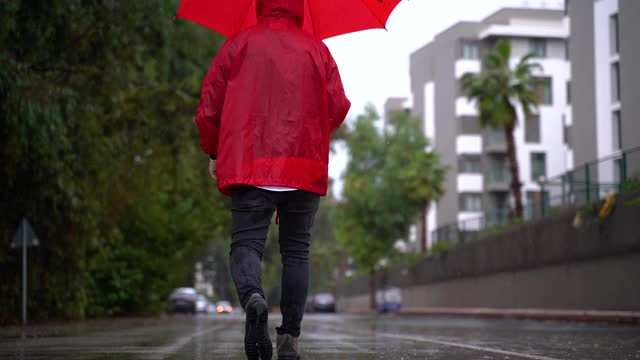 一个人穿着红色雨衣，拿着雨伞走在街上视频素材