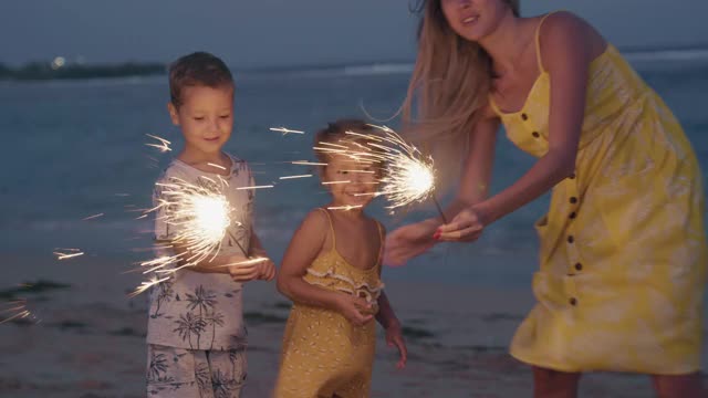 年轻的女人和她的孩子们在海边点亮闪光视频素材