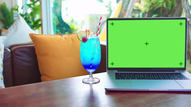 绿色屏幕的笔记本电脑坐在一个咖啡店的桌子上视频素材