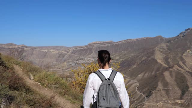 在一个秋高山晴的日子里，一名身穿白色衬衫、背着背包的年轻女子爬上了山路视频素材