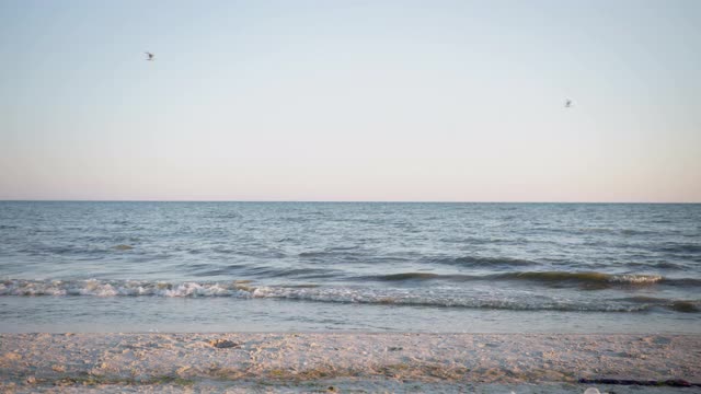 海边度假时，年轻美丽苗条的女孩们穿着泳衣，手牵着手沿着沙滩跑进水中，在夏日周末的天空和海浪的背景下视频素材