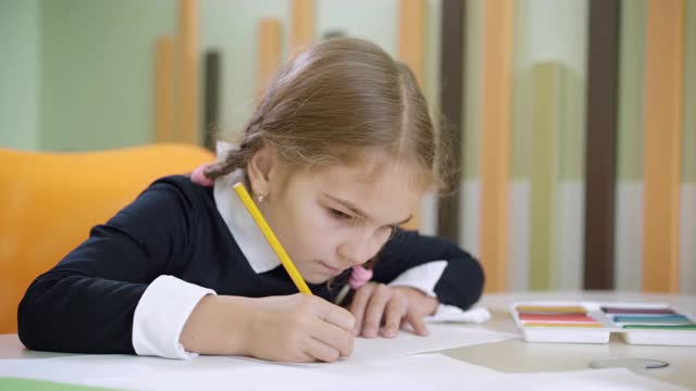 一个不开心的女孩在书桌上画画，把铅笔扔了。可爱的白人小女生在公立学校的美术课上遇到了问题。教育和学习。视频素材