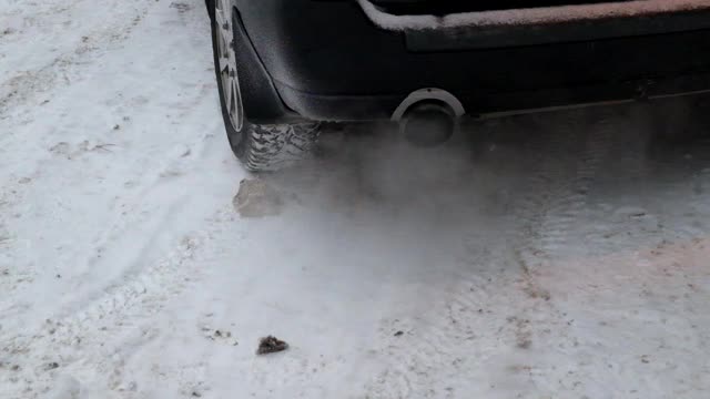 一辆停在雪地里的汽车的排气管和车轮。汽车启动后，废气从管道中排出。环境污染视频素材