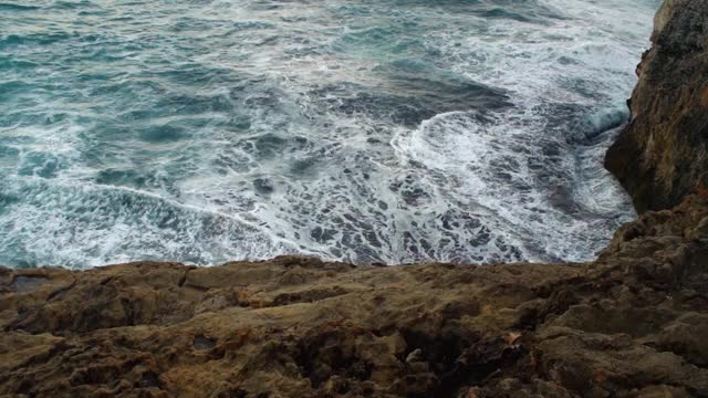 海浪拍打着岩石海岸，绿色的水溅起浪花，产生白色的泡沫，从上面看，慢动作视频视频素材