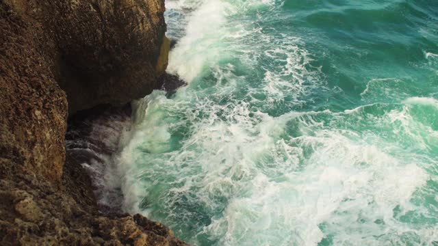 在一个阳光明媚的日子里，绿色海水中的小波浪拍打着岩石海岸，这是慢动作视频视频素材