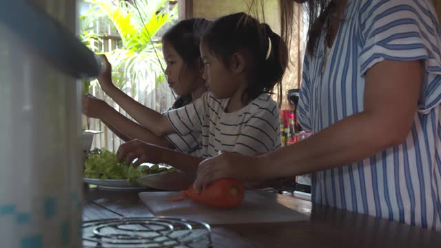 两个可爱的亚洲女孩和妈妈一起在厨房里准备食材，然后一起做蔬菜视频素材