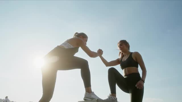 健身女性一起在立方体上锻炼——阳光明媚的日子里，强壮的女性运动员在万里无云的天空下进行健身训练，手牵手一起踩在立方体上视频素材