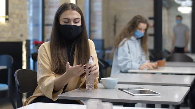 这位自信的年轻女子用洗手液消毒双手，摘下口罩，喝着美味的咖啡，面带微笑。美丽女士咖啡馆的肖像冠状病毒大流行。电影4k ProRes总部。视频素材