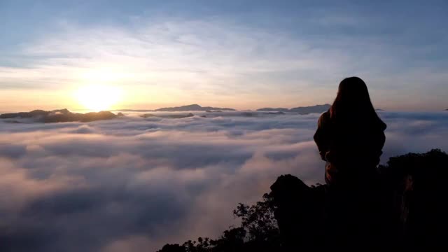 一个女旅行者坐在山顶上看日出和雾海的慢镜头视频素材