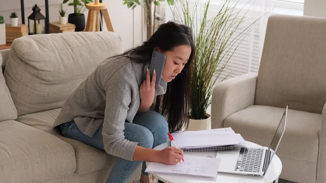 女人一边用笔记本电脑写笔记，一边用手机打电话视频素材