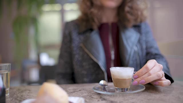 特写白种人年轻漂亮的女人喝一杯浓缩咖啡坐在一个酒吧。视频素材