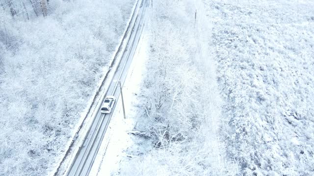 汽车在白雪覆盖的森林周围行驶的鸟瞰图视频素材