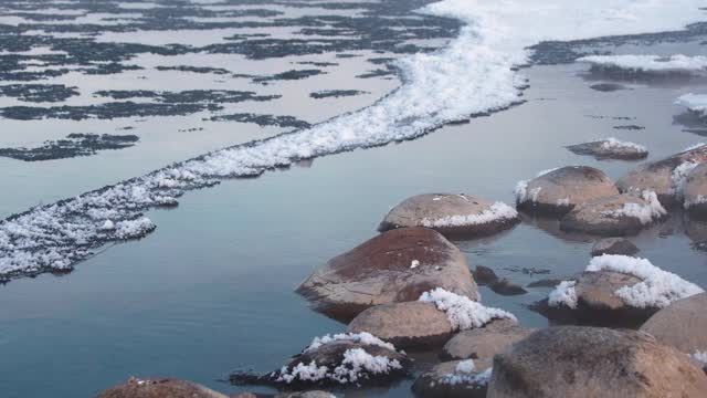 在晨雾笼罩下，冬天结冰的河流上的雪石视频素材