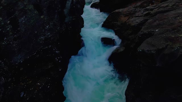 清澈的蓝色和冰冷的冰川河急流穿过陡峭崎岖的悬崖。视频素材