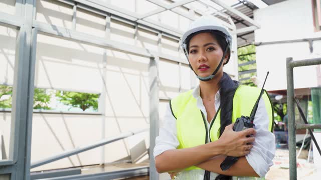 亚洲女工的肖像，人们戴着防护安全帽和眼镜现场的建筑。女工程师站在那里，交叉着胳膊，微笑着看着镜头。视频素材