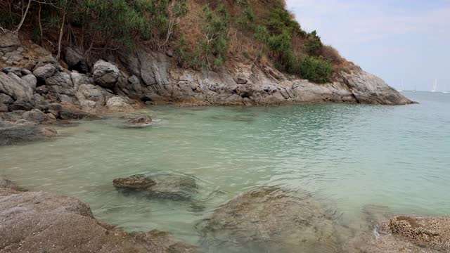 清澈、透明、绿松石般的海水。在普吉岛的海滩上，海浪撞击着巨大的岩石。背景是一块有树的岩石。视频素材